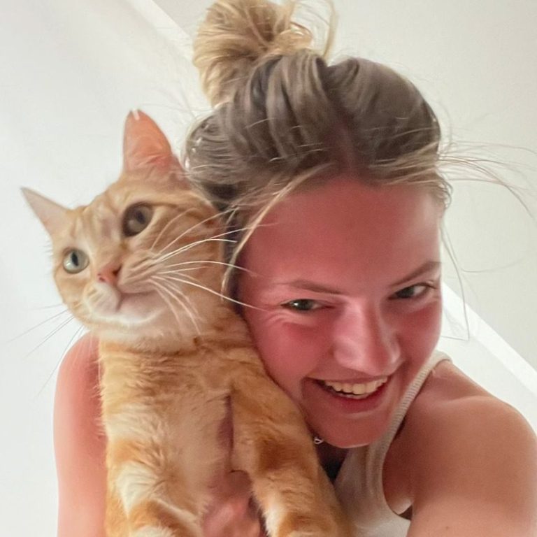 FAQ: Abgabesalon Ein hübsches, lächelndes Mädchen hält eine schmusende, orangefarbene Katze auf der Schulter.